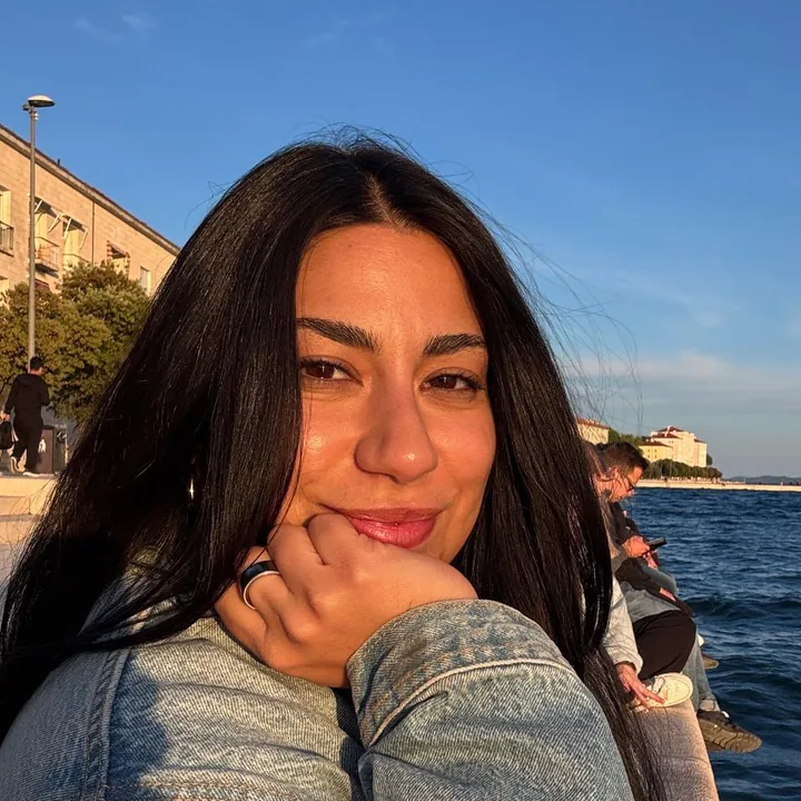 Mahdis, founder of Hava Workshops, resting her chin on her hand by the water at golden hour.