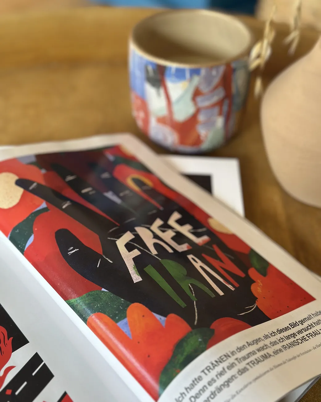 A magazine spread showing the founder&rsquo;s illustration &mdash; hand-painted figures in red, black and green with the words &lsquo;Free Iran&rsquo; lettered across it